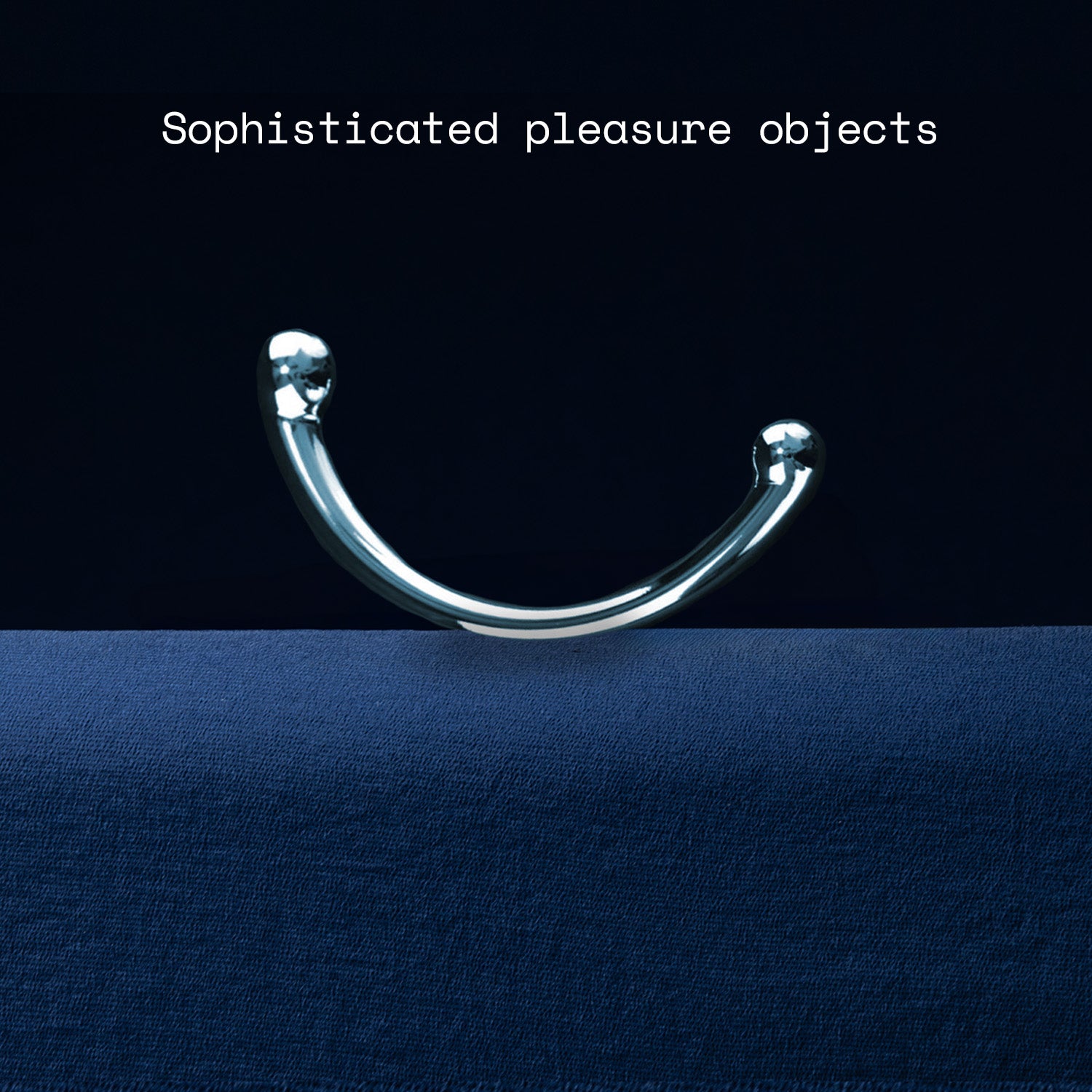 Metallic curved object on a dark blue fabric background with text 'Sophisticated pleasure objects'.