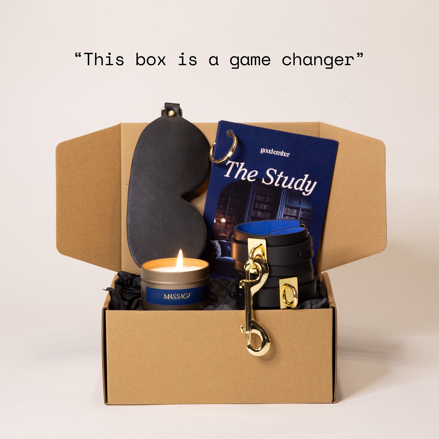 Open box containing a leather blindfold, booklet, leather cuffs and a massage candle. The quote reads 