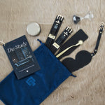 Sex toys displayed in a velvet bag. Italian leather handcuffs, Italian leather paddle, leather eye mask, massage candle, wartenberg wheel, hourglass, booklet.